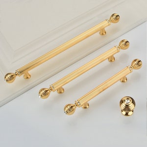 May include: Three gold cabinet pulls with a diamond-shaped design and a knob with a similar design. The pulls are 3 different sizes.