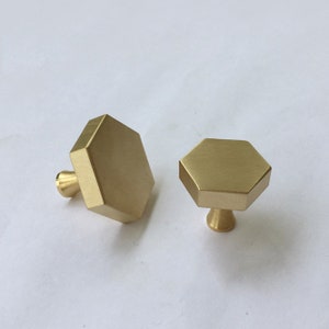 Può includere: Due pomelli esagonali dorati per armadi con finitura liscia. I pomelli sono in ottone massiccio e hanno un design semplice e moderno.