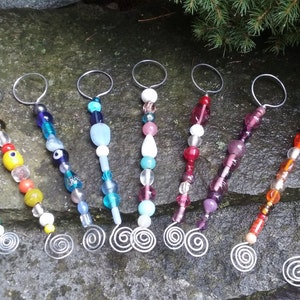May include: Ten colorful beaded keychains with silver wire loops. Each keychain features a variety of glass beads in different colors and patterns.