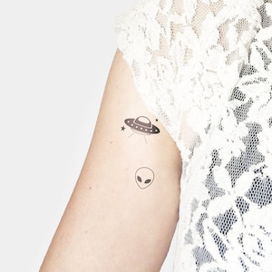 May include: A temporary tattoo featuring a black and white alien and a black and white UFO with stars.