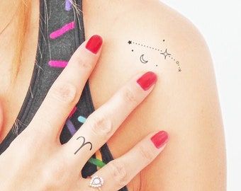 May include: A temporary tattoo with a constellation design featuring a crescent moon, stars, and a dotted line. The tattoo also includes the astrological symbol for Aries.
