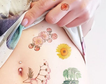 May include: A person's abdomen with several temporary tattoos of flowers and leaves. The tattoos are in shades of pink, yellow, green, and blue. There is a belly button piercing with a small silver ring.