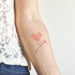 Peut inclure: Un motif de point de croix en forme de cœur rouge avec une aiguille et du fil. L'aiguille est enfilée avec du fil rouge et le fil sort du cœur.
