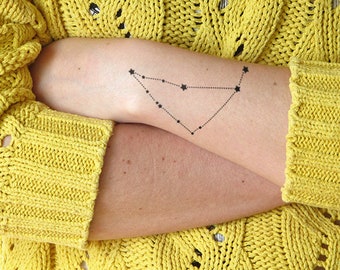 May include: A black temporary tattoo of the Capricorn constellation on a person's arm. The tattoo is a simple design of stars connected by lines.