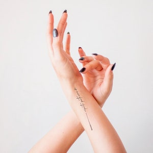 Könnte beinhalten: Ein Handgelenk mit einem schwarzen Tattoowortlaut "to-be-loved-is-to-be-free".