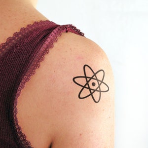 Puede incluir: Un tatuaje temporal negro de un átomo en el hombro de una persona.