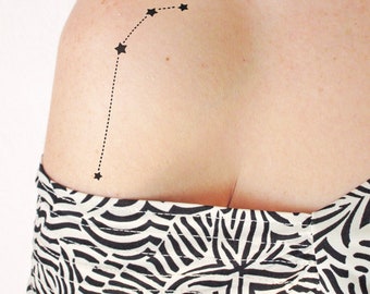 May include: A black constellation tattoo design with five stars connected by dotted lines on a person's shoulder.