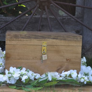 May include: A wooden box with a brass lock and key, surrounded by white flowers on a wooden surface.