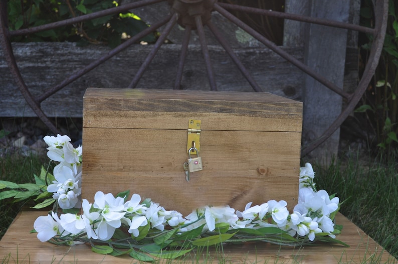 May include: A wooden box with a brass lock and key, surrounded by white flowers on a wooden surface.