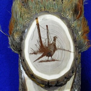 Peut inclure: Une plaque en bois avec un faisan brun grav&eacute; dans le bois. La plaque est entour&eacute;e d'un anneau de plumes de faisan.