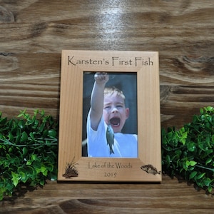 May include: A wooden photo frame with the text "Karsten's First Fish" and "Lake of the Woods 2019" engraved on it. The frame holds a photo of a young boy holding a fish.