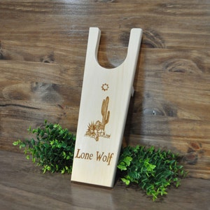May include: Wooden boot jack with a cactus and sun design and the text "Lone Wolf" engraved on the front.