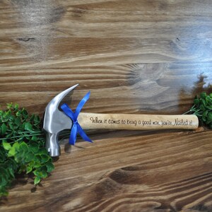 May include: A small silver hammer with a wooden handle. The handle is engraved with the text "When it comes to being a good man, you're Nailed it!" and tied with a blue ribbon.