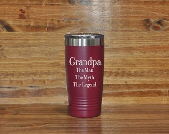May include: A maroon insulated tumbler with a silver rim and lid. The tumbler has the word "Grandpa" in white script, followed by "The Man. The Myth. The Legend." This travel mug is designed to keep beverages hot or cold.