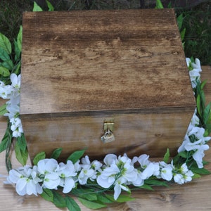 May include: A wooden box with a lock and key, decorated with a garland of white flowers and green leaves.