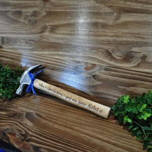 May include: A small wooden hammer with a silver head and a blue ribbon tied around the handle. The handle is engraved with the text "When it comes to being a good man, you've Nailed it!"