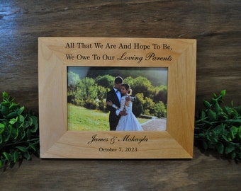 May include: A wooden picture frame with a personalized inscription: "All That We Are And Hope To Be, We Owe To Our Loving Parents." The frame features a wedding photo of a couple, with the names "James & Makayla" and the date "October 7, 2023" engraved below the photo.
