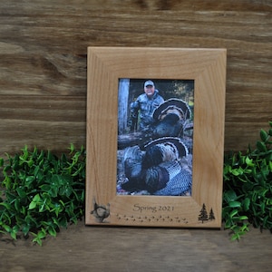 May include: A wooden picture frame with a photo of a person with a wild turkey. The frame has an engraved design of a turkey and the text "Spring 2021".