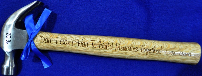 May include: A 16 ounce hammer with a wooden handle. The handle is engraved with the text "Dad, I Can't Wait To Build Memories Together! Love, Cora".
