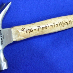 May include: A silver hammer with a wooden handle. The handle is engraved with the text "Pops - Thank You For Helping Me Build My Life".