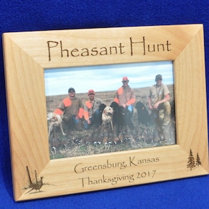 May include: A wooden picture frame with a photo of a group of people hunting pheasants. The frame is engraved with the words "Pheasant Hunt", "Greensburg, Kansas", and "Thanksgiving 2017".