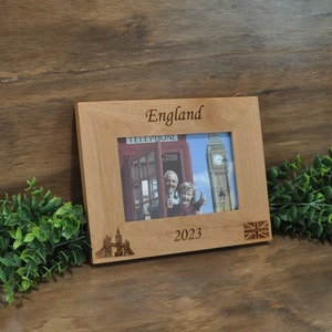 May include: A wooden photo frame with an engraved design featuring a red telephone booth, Big Ben, and the Union Jack flag. The frame has the words "England" and "2023" engraved on it.