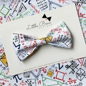 Può includere: Un papillon bianco con un motivo ripetuto di equazioni e simboli matematici. Il papillon è su una carta color crema con il testo "Little Beau boutique" e "HIGH QUALITY, HAND CRAFTED BOW TIES FOR ALL AGES."