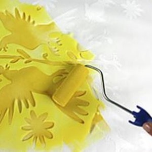 Puede incluir: Un rodillo de pintura amarillo se est&aacute; utilizando para aplicar pintura amarilla a una plantilla de dos p&aacute;jaros y una flor. La plantilla est&aacute; sobre una superficie blanca.