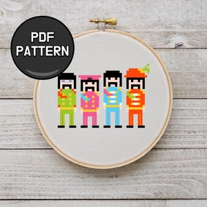 May include: A cross-stitch pattern in an embroidery hoop. The design shows four pixelated figures in colourful uniforms. The text "PDF PATTERN" is in a black circle at the top. The figures are in green, pink, blue, and orange.