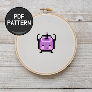 May include: A cross-stitch pattern displayed in a wooden embroidery hoop. The design features a pixelated purple creature with black arms and legs. A black circle with the words "PDF PATTERN" is in the upper left corner.