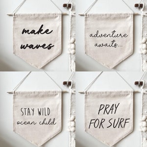 May include: Four beige canvas banners with black text. The banners read "make waves", "adventure awaits", "stay wild ocean child", and "pray for surf".