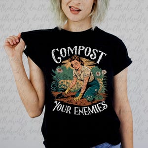 Puede incluir: Camiseta negra con un gráfico de estilo vintage. El diseño muestra a una mujer jardinería con el texto "COMPOST YOUR ENEMIES" en blanco, con una fuente desgastada. El diseño incluye flores y una escena de jardinería.