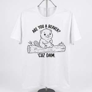 Könnte beinhalten: Ein weißes kurzärmeliges T-Shirt mit einer schwarzen Strichzeichnung eines Bibers, der auf einem Baumstamm sitzt. Der Text über dem Biber lautet ARE YOU A BEAVER? und der Text unter dem Baumstamm lautet 'CUZ DAM. Das Motiv ist mittig platziert.