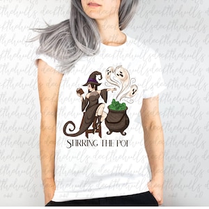 May include: White t-shirt featuring a witch illustration. The witch is wearing a hat and holding a book, with a cauldron and ghosts. The text "STIRRING THE POT" is below the illustration.