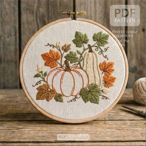 Könnte beinhalten: Ein Stickrahmen mit einem herbstlichen Design. Die Stickerei zeigt zwei Kürbisse, einen runden und einen länglichen, umgeben von orangefarbenen, braunen und grünen Blättern. Der Text "PDF PATTERN" ist sichtbar.