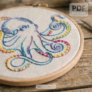 May include: Embroidered octopus design in a wooden hoop. The octopus is stitched with blue, purple, and rainbow-colored thread. The text "PDF PATTERN" is in the upper right corner, with additional text below. The Crafty Studio logo is at the bottom.