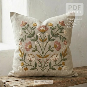 Puede incluir: Cojín de lino beige con un diseño floral bordado. El bordado presenta flores rosas, amarillas y blancas con hojas verdes. El cojín tiene el texto "PDF PATTERN" y "+ thread colour suggestions + list of the stitches".