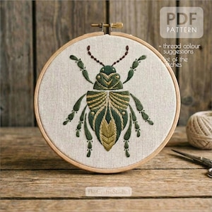 Könnte beinhalten: Ein besticktes Insektenmuster in einem Holzrahmen. Der Käfer ist mit grünen und goldenen Fäden auf beigem Stoff detailliert. Der Text "PDF PATTERN" ist sichtbar, zusammen mit dem Text "+ thread colour suggestions list of the stitches".