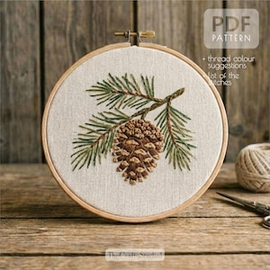 May include: Embroidered pine cone and branch design in a wooden embroidery hoop. The artwork features brown and green thread on a beige fabric. The text "PDF PATTERN" is visible, along with additional text. The Crafty Studio logo is at the bottom.