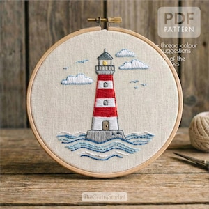 May include: Embroidered lighthouse design in a wooden hoop. The lighthouse is red and white, with blue waves and clouds. The text "PDF PATTERN" is visible. The Crafty Studio logo is at the bottom.