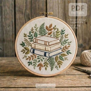 May include: Embroidered hoop art featuring a stack of three books surrounded by green, brown, and gold leaves. The design is stitched on a cream-colored fabric and framed in a wooden hoop. Text on the image reads "PDF PATTERN".