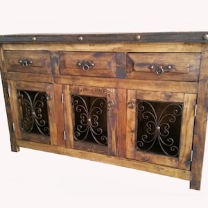 May include: A rustic wooden cabinet with three drawers and three doors. The doors have a wrought iron design and the cabinet has a distressed finish.