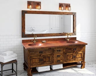 Può includere: Un mobile da bagno rustico con un grande specchio, due lavandini e un mobile in legno. Il mobile ha un piano di lavoro in rame e rubinetti in ottone. Due applique abbinate con luci a gabbia sono montate sopra lo specchio.