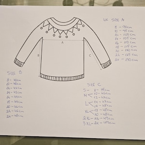 May include: A hand-drawn diagram of a sweater with measurements for different sizes labeled "UK Size A", "Size B", and "Size C". The diagram shows the length, width, and sleeve length of the sweater.