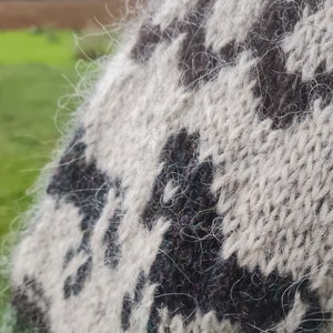 May include: Close-up of a white and black knitted sweater with a fuzzy texture. The sweater has a geometric pattern.