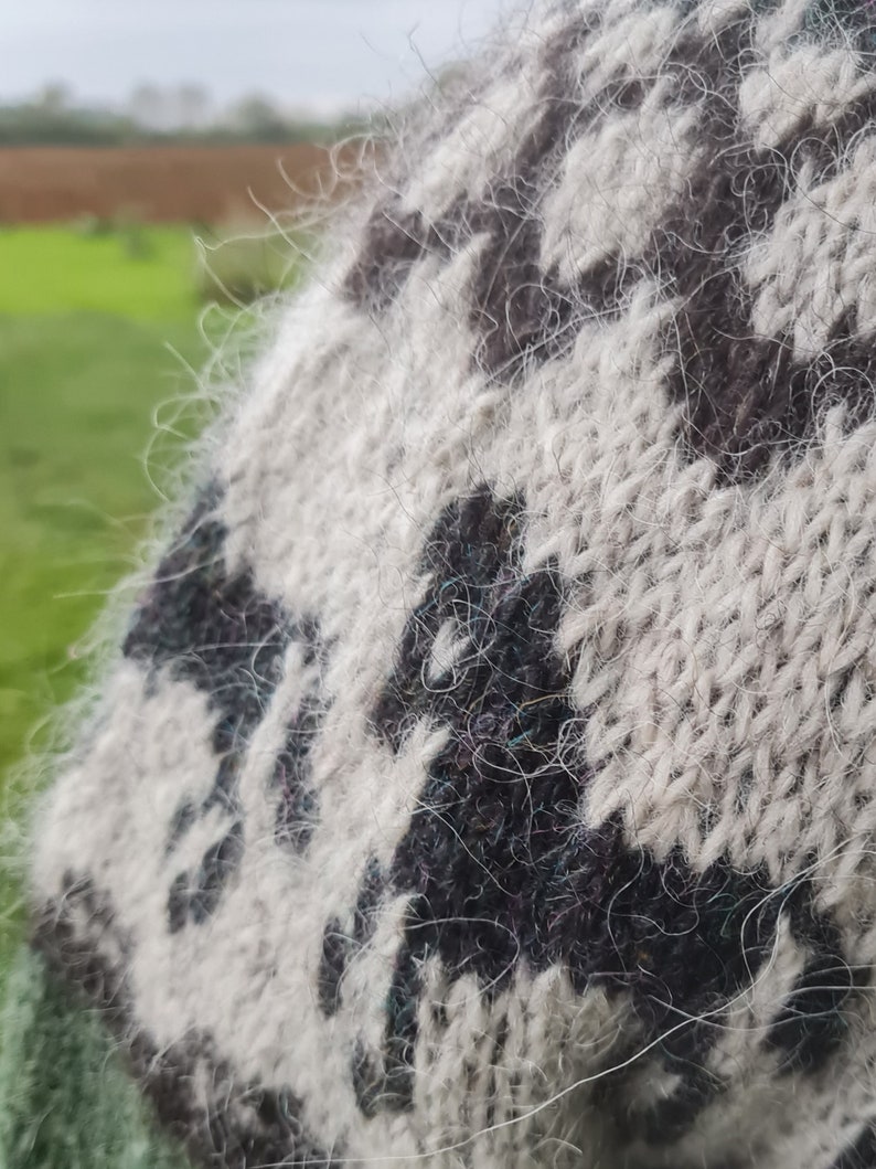 May include: Close-up of a white and black knitted sweater with a fuzzy texture. The sweater has a geometric pattern.