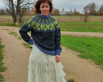 May include: A woman wearing a blue and green patterned sweater with a white, layered tulle skirt and brown boots. She is standing on a dirt path with green grass on either side.