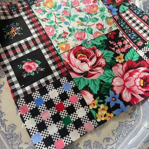 Op de afbeelding: Een vierkante stoffen lap met een patchworkontwerp van diverse bloemen- en geometrische patronen. De stof bevat zwarte, witte, rode, roze, groene en blauwe kleuren met rozenmotieven, geblokte vierkanten en kleine veelkleurige stippen.