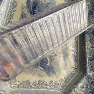 May include: A clear glass rectangular dish with a ribbed design. The dish is sitting on a blue and white patterned surface.