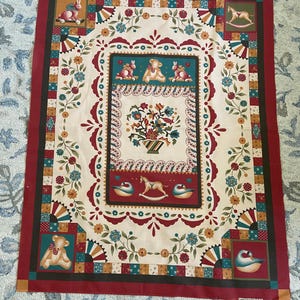 May include: A decorative fabric panel featuring a central rectangular design with a vase of flowers. The panel has a cream background with a red border and colorful squares. The design includes teddy bears, bunnies, and rocking horses.